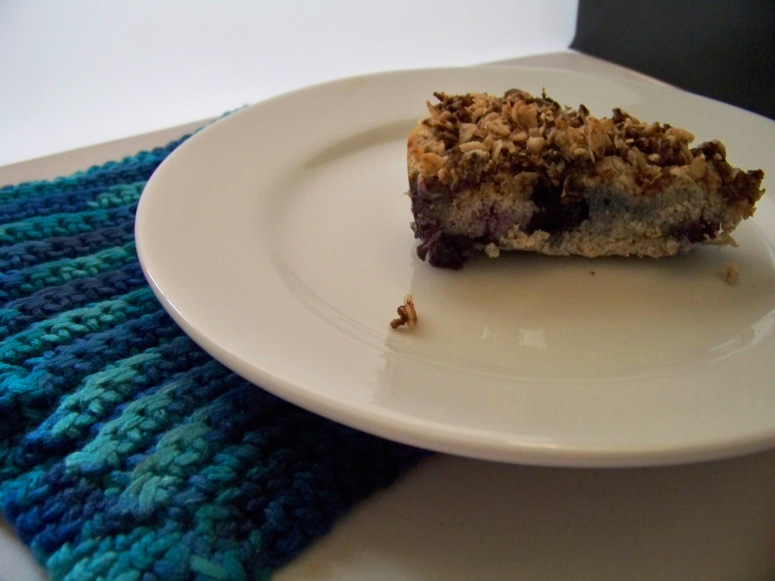 Plated blueberry buckle dessert on white plate with a potholder in shades of blue underneath the left side