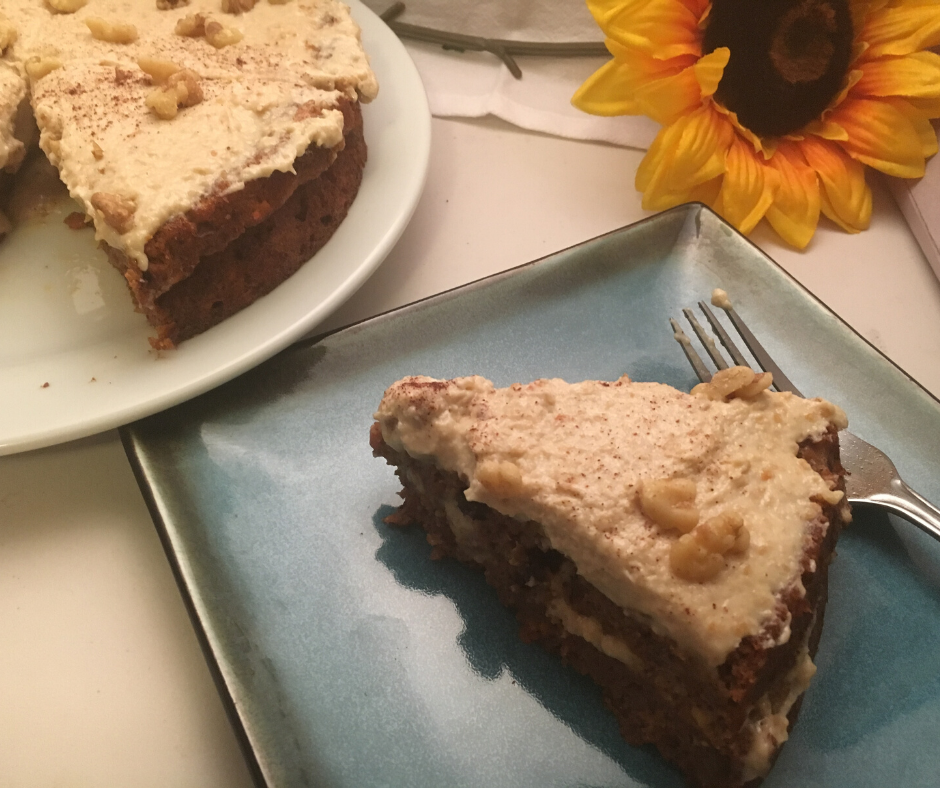 Dairy Free Coconut Carrot Cake, a slice on a square blue plate with the remaining cake slightly visible on a white round plate in the back left with a sunflower filling the remaining top of the image