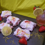 Strawberry Lemonade Bars sliced on a cookie sheet with a glass of lemonade to the back right with whole strawberries around the bars